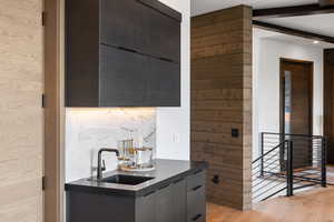 Bar area featuring modern cabinets, light wood-type flooring, dark stone counters, decorative backsplash, and beamed ceiling