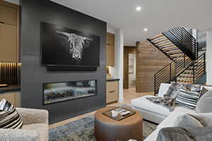 Living area featuring a glass covered fireplace, light wood-type flooring, stairway, and recessed lighting