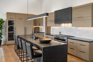 Kitchen featuring modern cabinets, a kitchen island with sink, a breakfast bar area, decorative backsplash, and pendant lighting