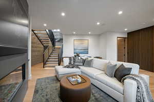 Living area with recessed lighting, light wood-type flooring, a glass covered fireplace, stairway, and wooden walls