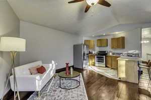 Living area featuring vaulted ceiling, ceiling fan, and light wood-style flooring