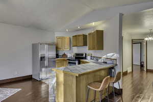 Kitchen with a peninsula, a breakfast bar, stainless steel appliances, tile countertops, and dark wood-style flooring