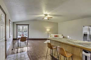 Kitchen with tile counters, a kitchen bar, stainless steel fridge with ice dispenser, vaulted ceiling, and light wood finished floors