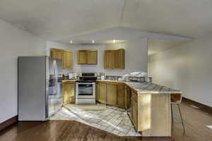 Kitchen with stainless steel appliances, brown cabinets, a breakfast bar area, tile countertops, and a peninsula