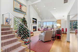 Living room with high vaulted ceiling, a warm lit fireplace, light wood finished floors, recessed lighting, and stairway