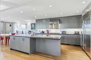 Kitchen with gray cabinets, a kitchen island with sink, recessed lighting, stainless steel appliances, and light wood-type flooring