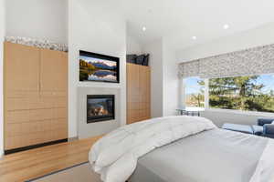 Bedroom featuring a glass covered fireplace, wood finished floors, recessed lighting, and vaulted ceiling