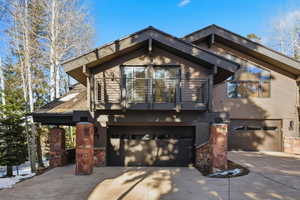 View of front of home featuring a balcony, stone siding, driveway, and a garage