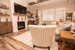 Living room featuring a glass covered fireplace, light wood-type flooring, and beam ceiling