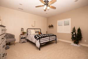 Bedroom with a decorative wall, light colored carpet, and ceiling fan