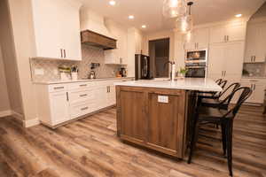 Kitchen with premium range hood, white cabinets, a kitchen island with sink, and recessed lighting