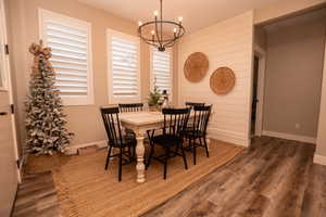 Dining space featuring dark wood-style flooring, a chandelier, and wood walls