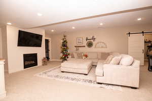 Living area featuring a barn door, a fireplace, light carpet, and recessed lighting