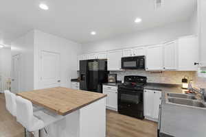 Kitchen featuring black appliances, white cabinetry, tasteful backsplash, a kitchen bar, and wooden counters