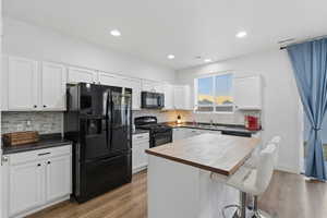 Kitchen featuring black appliances, white cabinetry, a breakfast bar area, a kitchen island, and backsplash