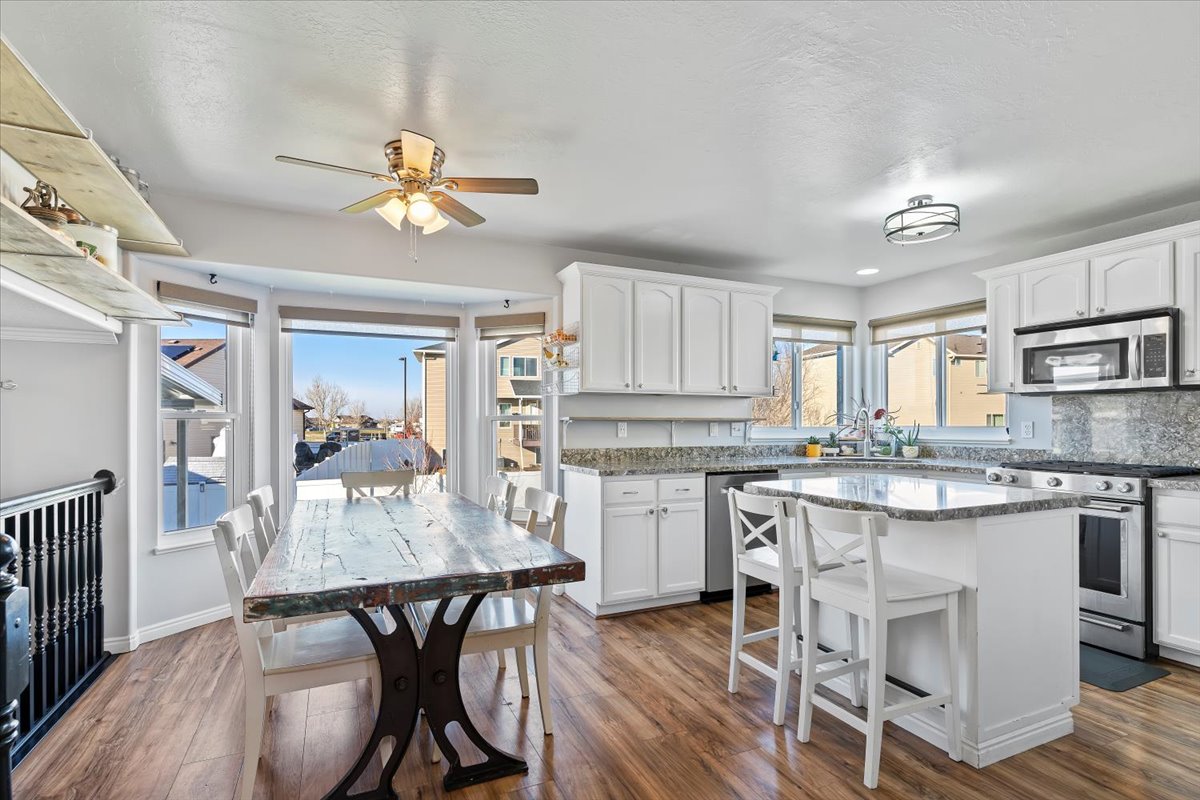 Kitchen featuring appliances with stainless steel finishes, quartz countertops, white cabinetry, a kitchen bar, and dark wood-style flooring