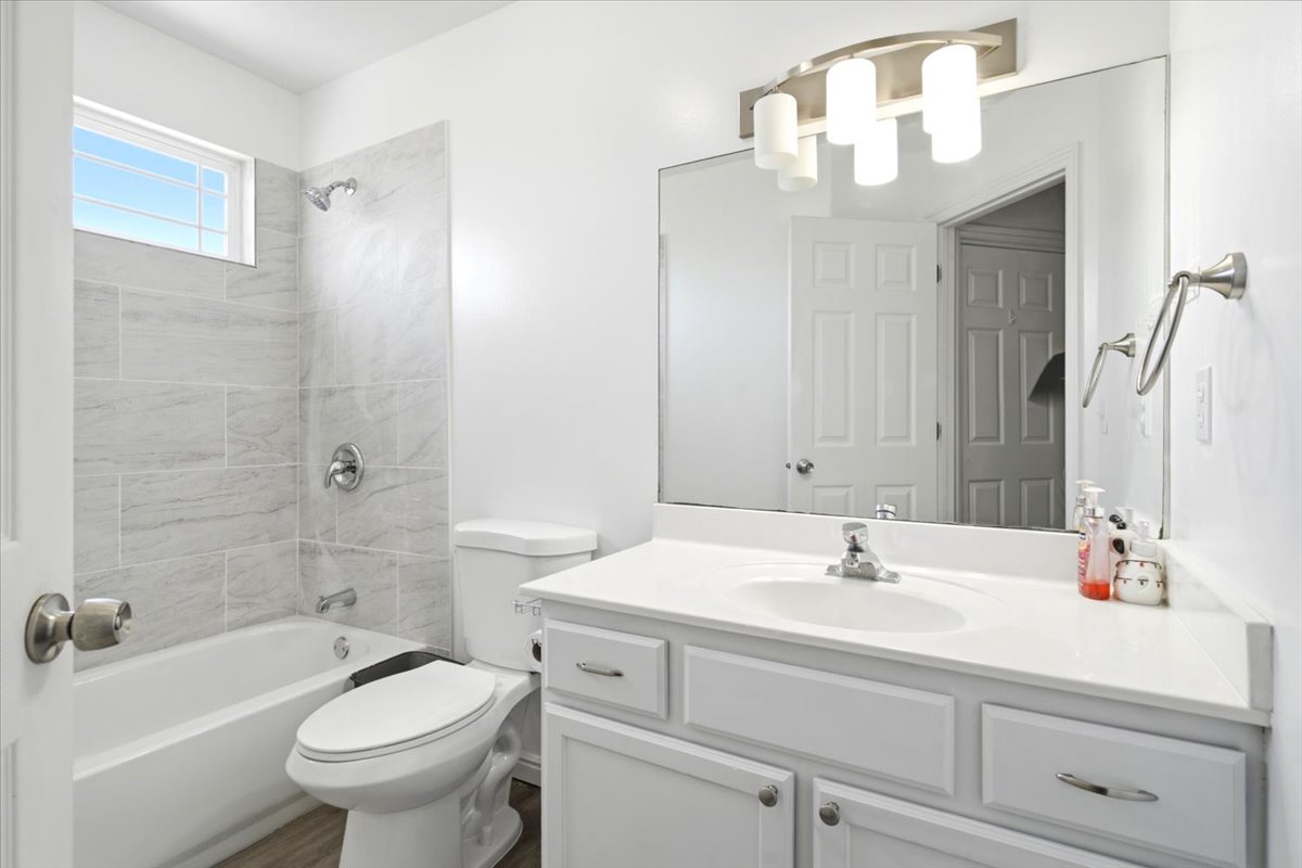 Full bathroom featuring a white vanity with integrated sink, a large wall-mounted mirror, brushed nickel light fixture, and a tub/shower combination with light grey subway tile surround