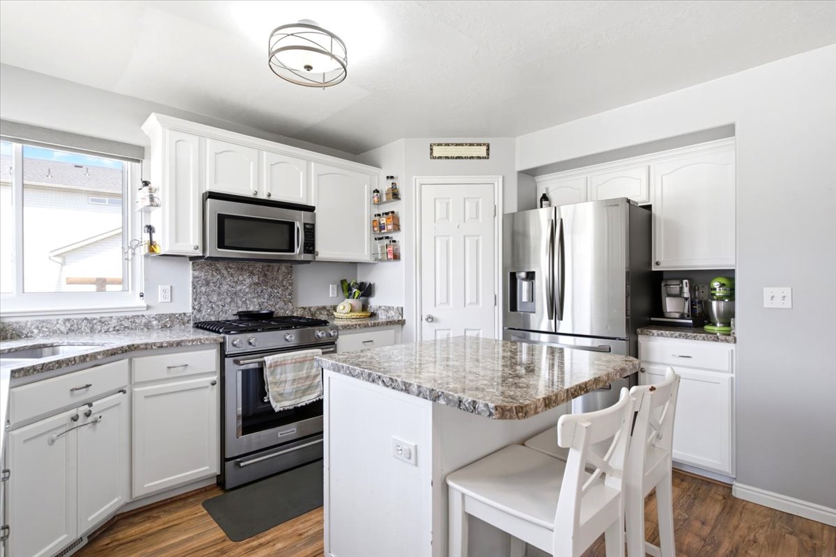 Bright kitchen featuring white cabinetry, stainless steel appliances, speckled countertops, and wood-finish flooring