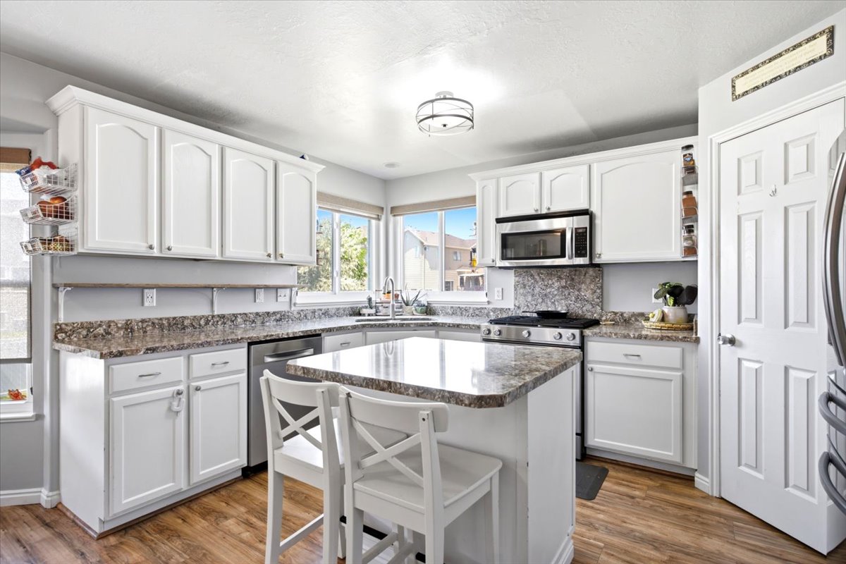 Kitchen featuring white cabinetry, stone-finish countertops, stainless steel appliances, a central island, and wood-finish flooring