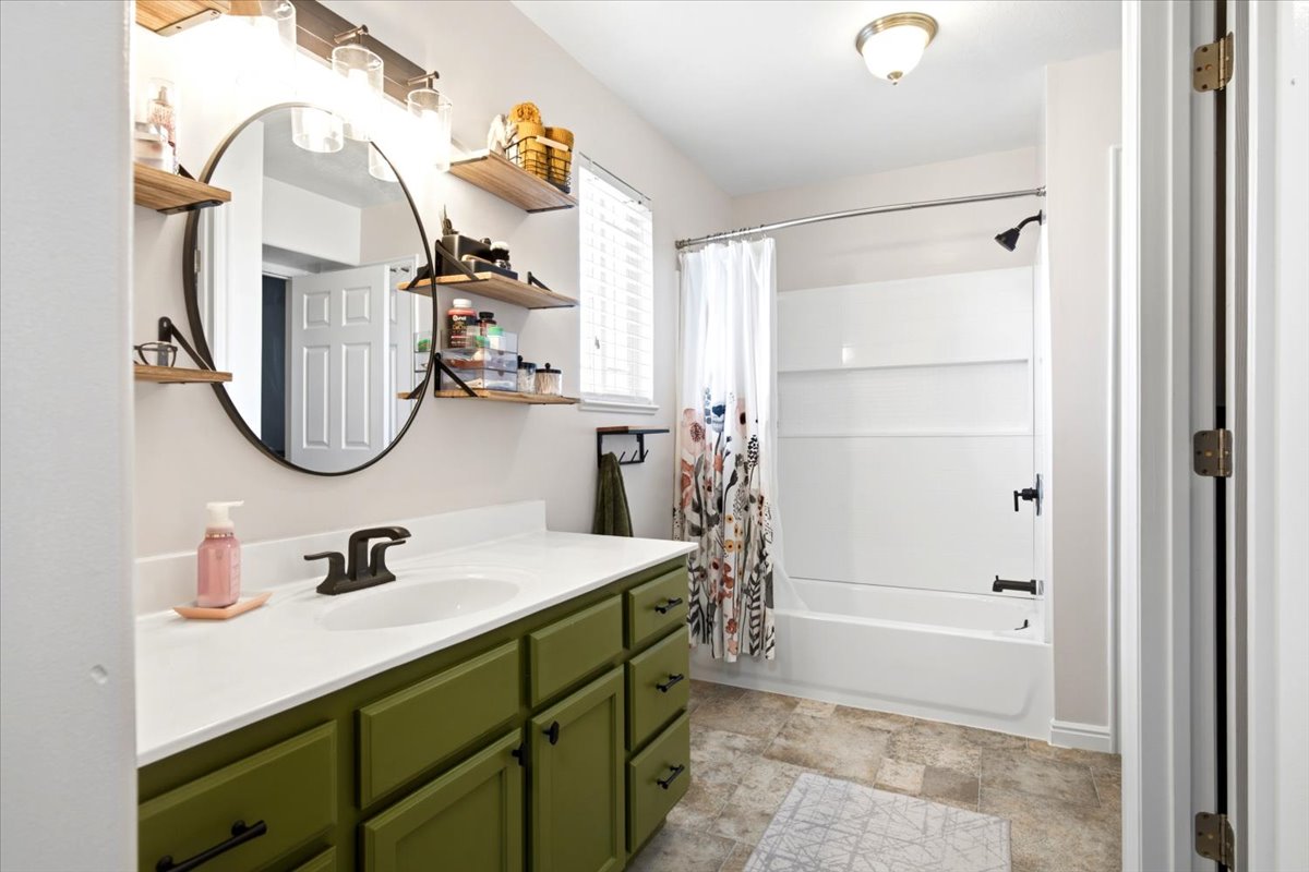 Bathroom featuring a green vanity with a white countertop, a circular mirror, and a built-in shower/tub combination with matte black fixtures