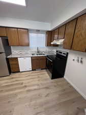 Kitchen featuring stainless steel appliances, brown cabinetry, light wood finished floors, and light countertops