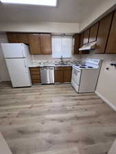 Kitchen featuring white appliances, light countertops, light wood finished floors, under cabinet range hood, and brown cabinetry