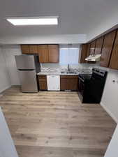 Kitchen featuring light countertops, freestanding refrigerator, electric range oven, light wood finished floors, and white dishwasher