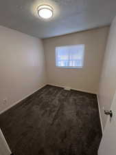 Empty room featuring a textured ceiling and dark carpet
