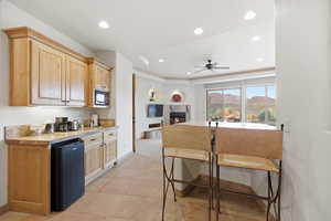 Kitchen featuring black appliances, a fireplace, light brown cabinets, recessed lighting, and a breakfast bar area