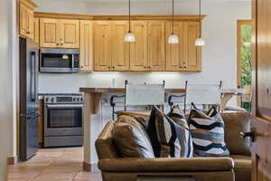 Kitchen featuring stainless steel appliances, hanging light fixtures, dark countertops, open floor plan, and light brown cabinetry