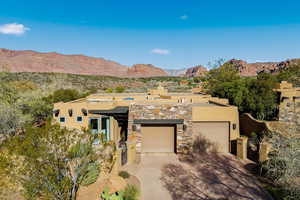 Pueblo-style home with stucco siding, a mountain view, concrete driveway, a garage, and stone siding