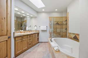 Bathroom with double vanity, a skylight, a stall shower, a bath, and recessed lighting