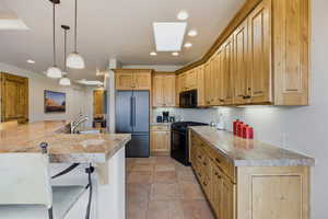 Kitchen with black appliances, light countertops, pendant lighting, a skylight, and a breakfast bar