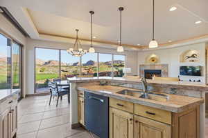 Kitchen with hanging light fixtures, a tile fireplace, stainless steel dishwasher, an island with sink, and a chandelier
