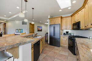 Kitchen featuring black appliances, decorative light fixtures, light brown cabinetry, a skylight, and a kitchen breakfast bar