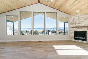 Unfurnished living room featuring a mountain view, a stone fireplace, light wood-style floors, vaulted ceiling, and wooden ceiling