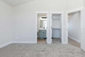 Unfurnished bedroom with a spacious closet, light carpet, and ensuite bathroom