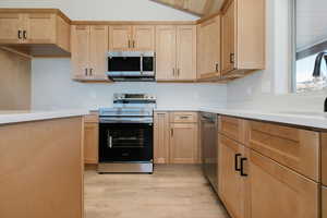 Kitchen featuring light brown cabinets, stainless steel appliances, and lofted ceiling