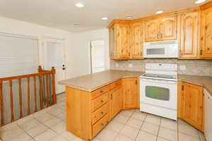 Kitchen with white appliances, a peninsula, light countertops, tasteful backsplash, and recessed lighting