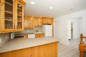 Kitchen with glass insert cabinets, light countertops, white appliances, tasteful backsplash, and a peninsula