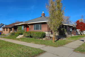 View of front of property featuring brick siding, a front yard, a chimney, and roof with shingles