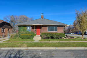 Bungalow-style house with roof with shingles, a chimney, and a front lawn