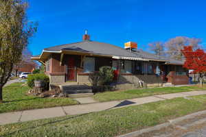Bungalow-style home featuring a chimney, a front lawn, a shingled roof, and brick siding