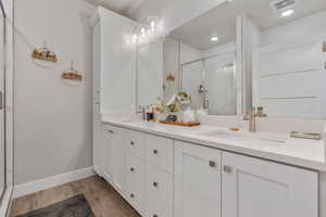 Full bath with double vanity, a marble finish shower, and light wood-style flooring