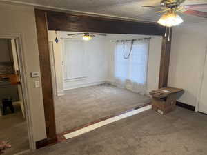 Unfurnished living room featuring ceiling fan, carpet floors, and a textured wall