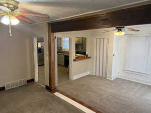 Empty room with ceiling fan, dark colored carpet, and a textured ceiling