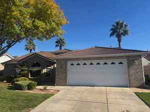 View of front facade featuring brick siding, concrete driveway, an attached garage, a front yard, and a tile roof