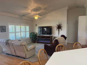 Living room with ornamental molding, vaulted ceiling, wood finished floors, and a ceiling fan