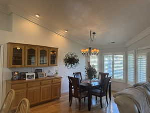 Dining room featuring crown molding, light wood-type flooring, vaulted ceiling, and a chandelier