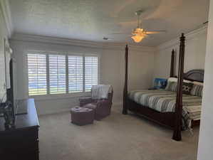 Bedroom featuring a textured ceiling, light carpet, ornamental molding, and ceiling fan